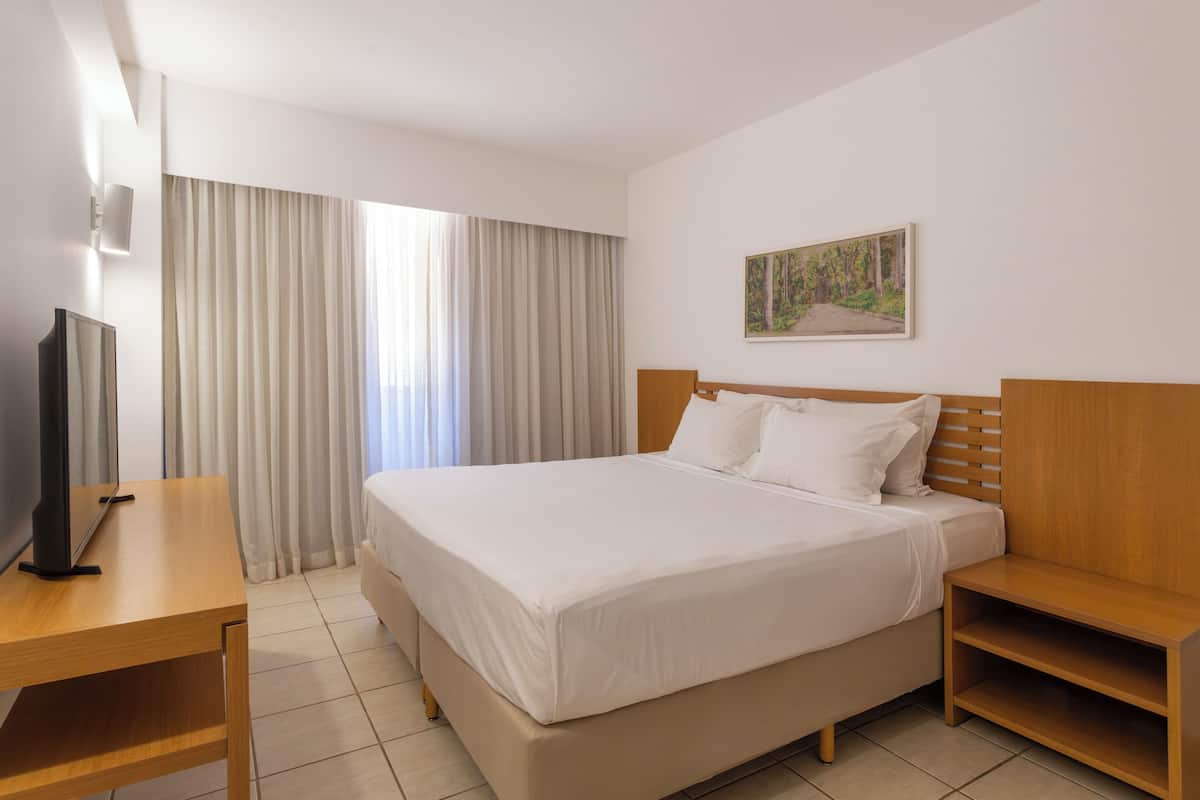 A hotel room with a bed, a desk, a TV, and a painting on the wall.