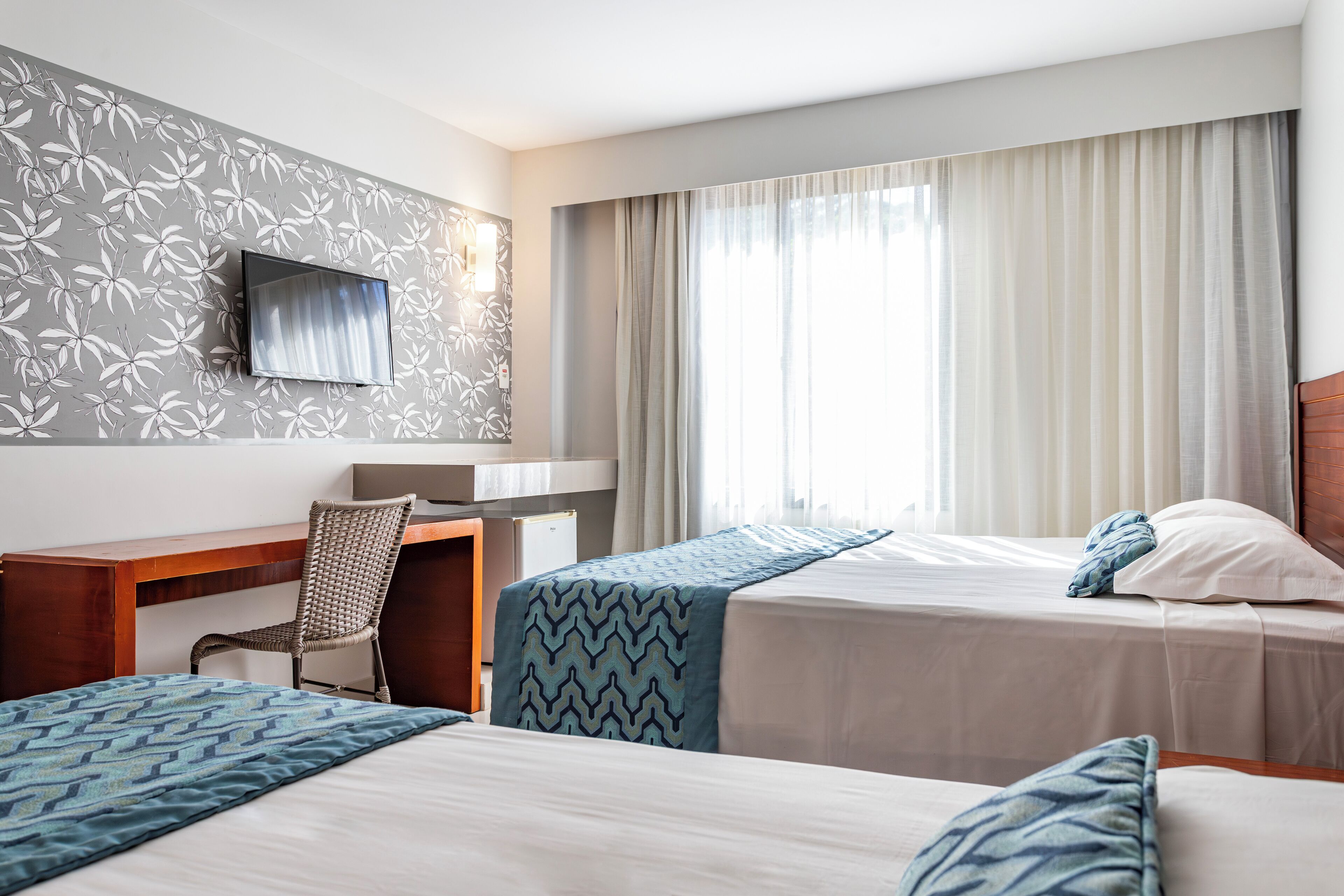 A hotel room with two beds, a desk, a chair, a TV, and curtains.