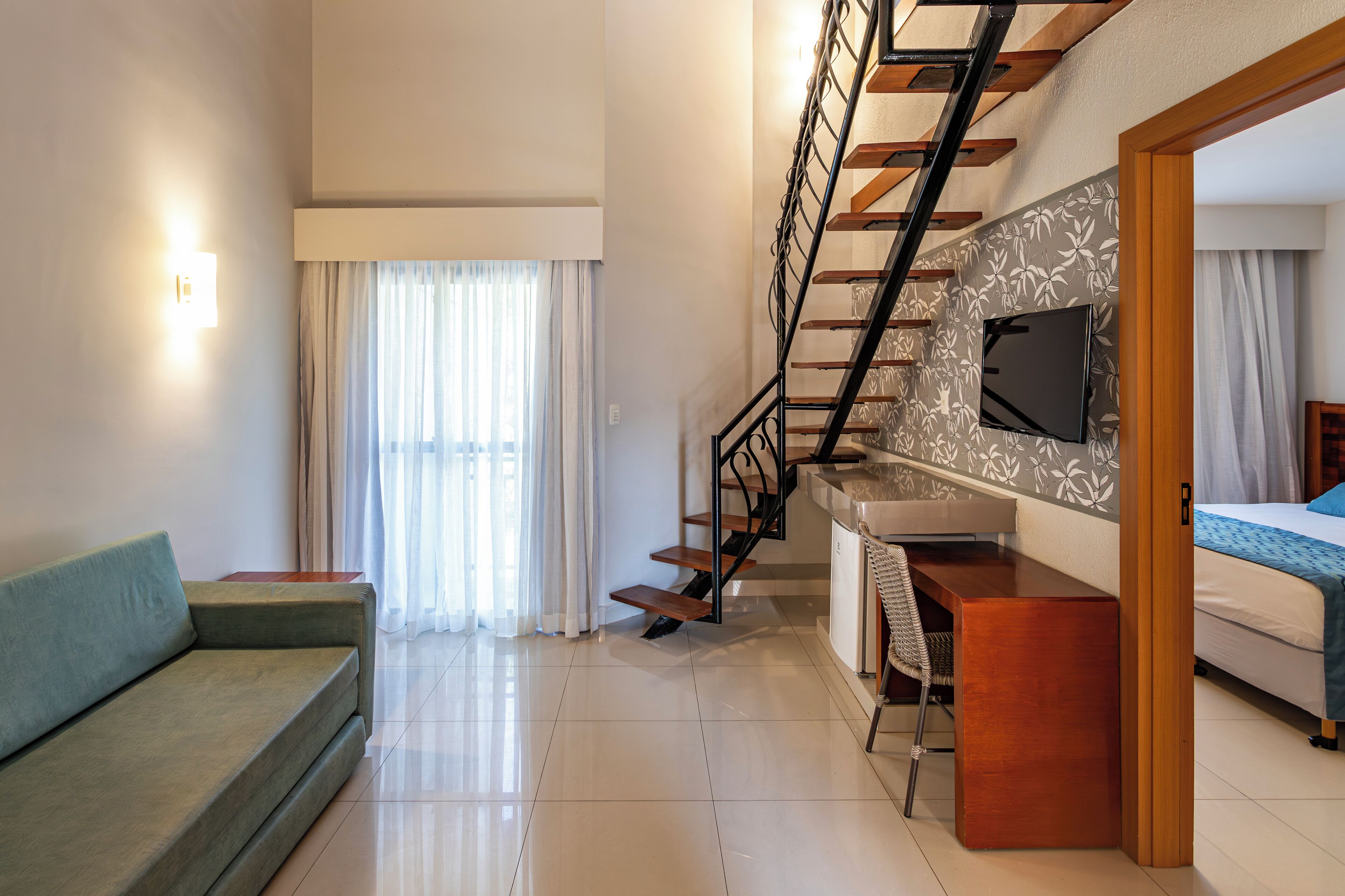 A modern living room with a sofa, a staircase, a desk, and a bed.