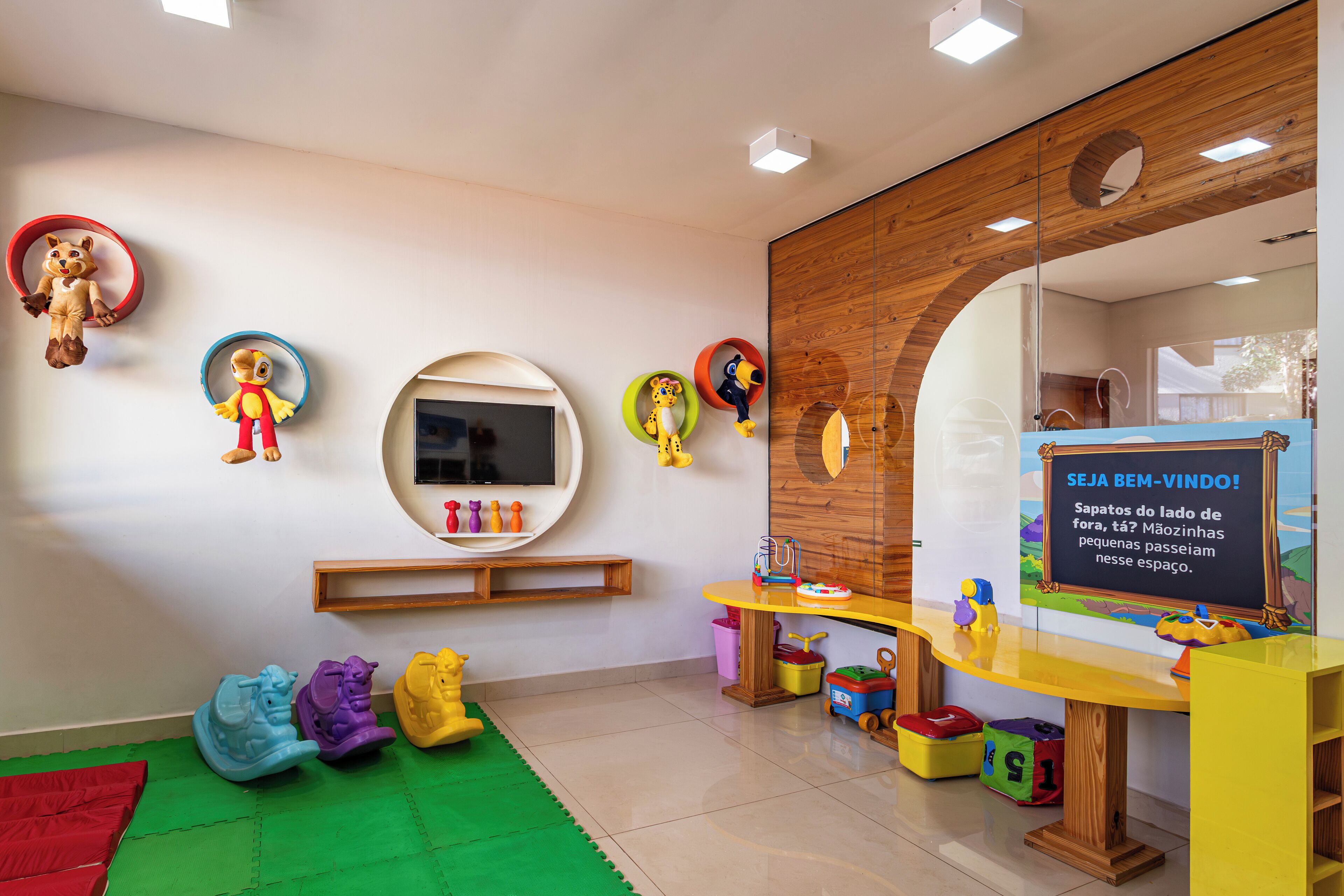 A children's playroom with a large mirror, colorful toys, and a chalkboard with writing.