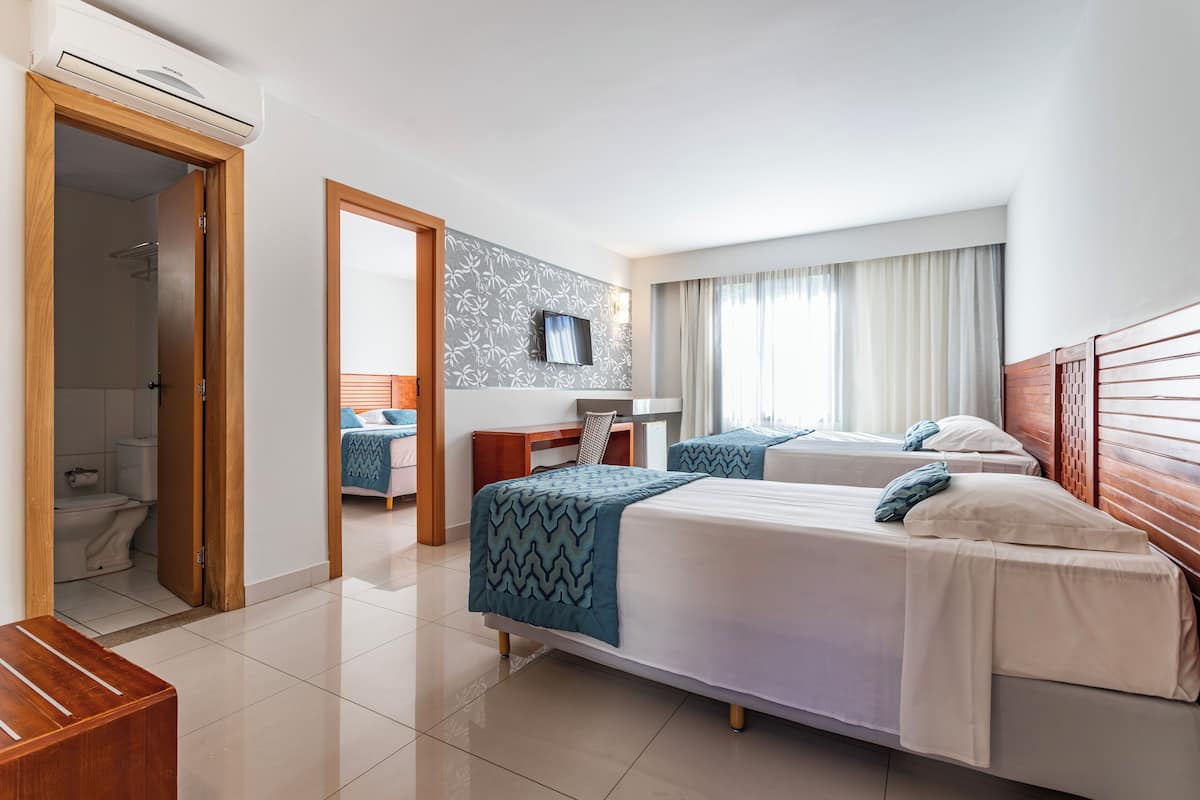 A hotel room with two beds, a desk, a TV, and a bathroom.