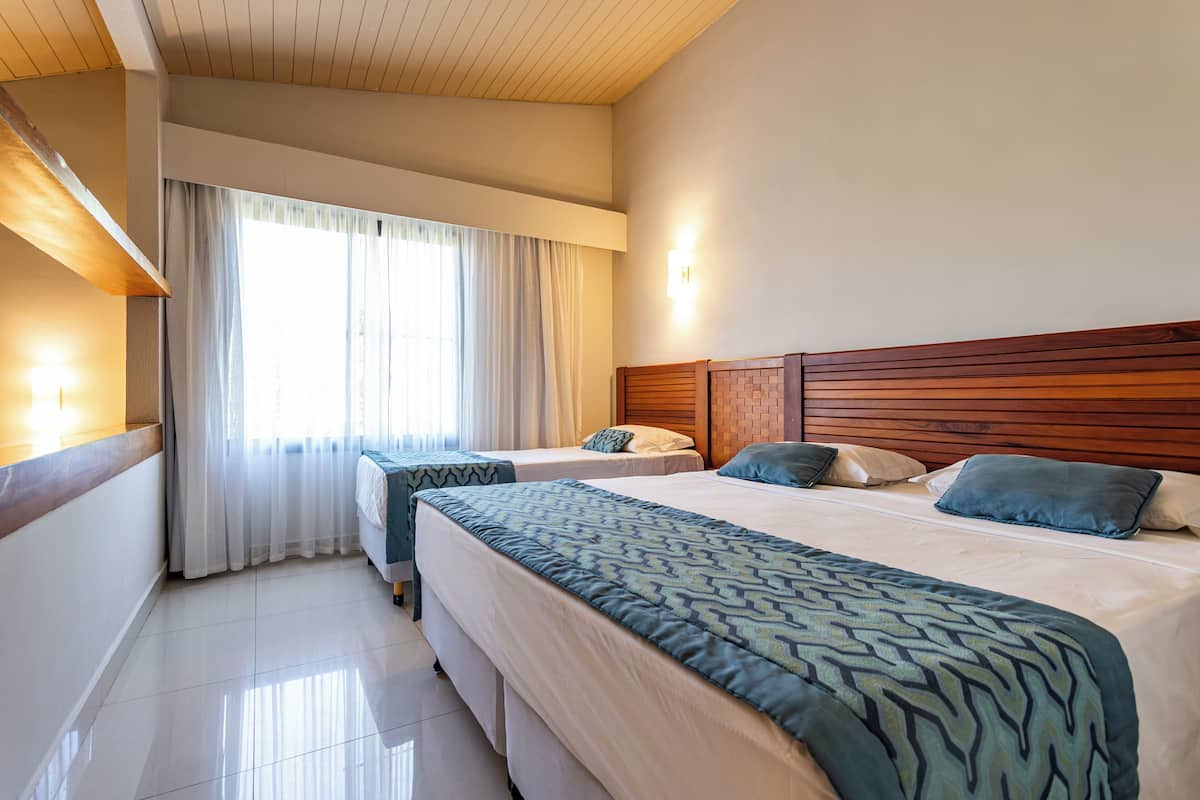 A hotel room with two beds, wooden headboards, and a large window with curtains.
