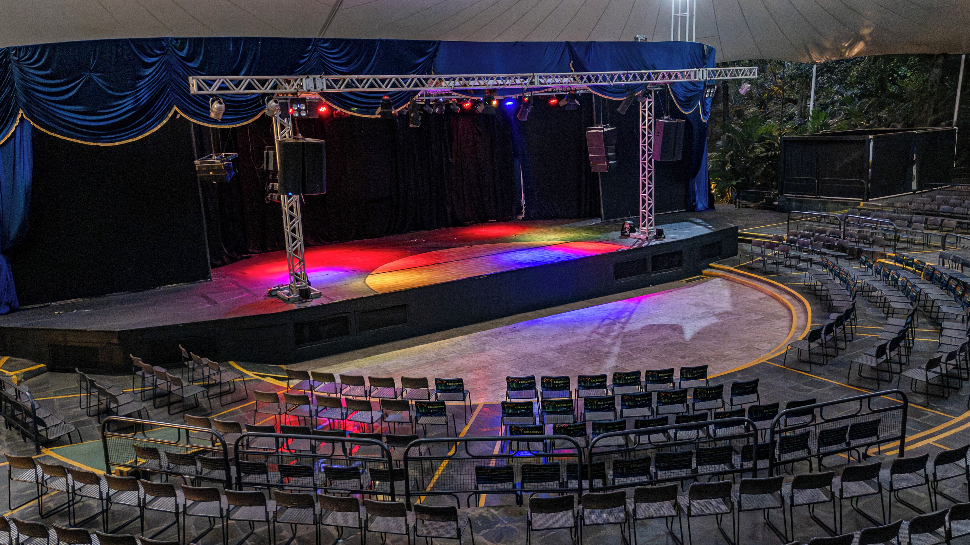 Un anfiteatro al aire libre con asientos escalonados y un escenario equipado con sistemas de iluminación y sonido.