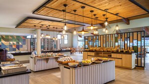 A modern breakfast area with wooden flooring, a central island with bowls of fruit and pastries, and hanging pendant lights. - Rio Quente Resorts - Hotel Luupi (Rio Quente)
