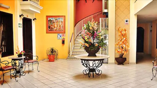 Eine Hotelhalle mit Fliesenboden, einem runden Tisch in der Mitte mit Blumenarrangement und zwei Blumentöpfen.