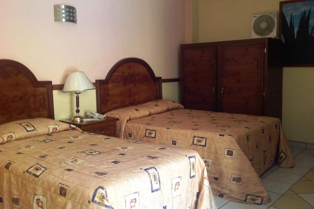 Un dormitorio con dos camas, una mesita de noche con lámpara, un armario y un equipo de aire acondicionado.