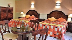 Ein Hotelzimmer mit zwei Betten, einem Holzschrank, einem runden Tisch mit Stühlen und zwei Nachttischlampen.