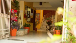 Ein Hotelzugang mit einer Treppe zum Obergeschoss, Zimmerpflanzen und einem Feuerlöscher an der Wand.