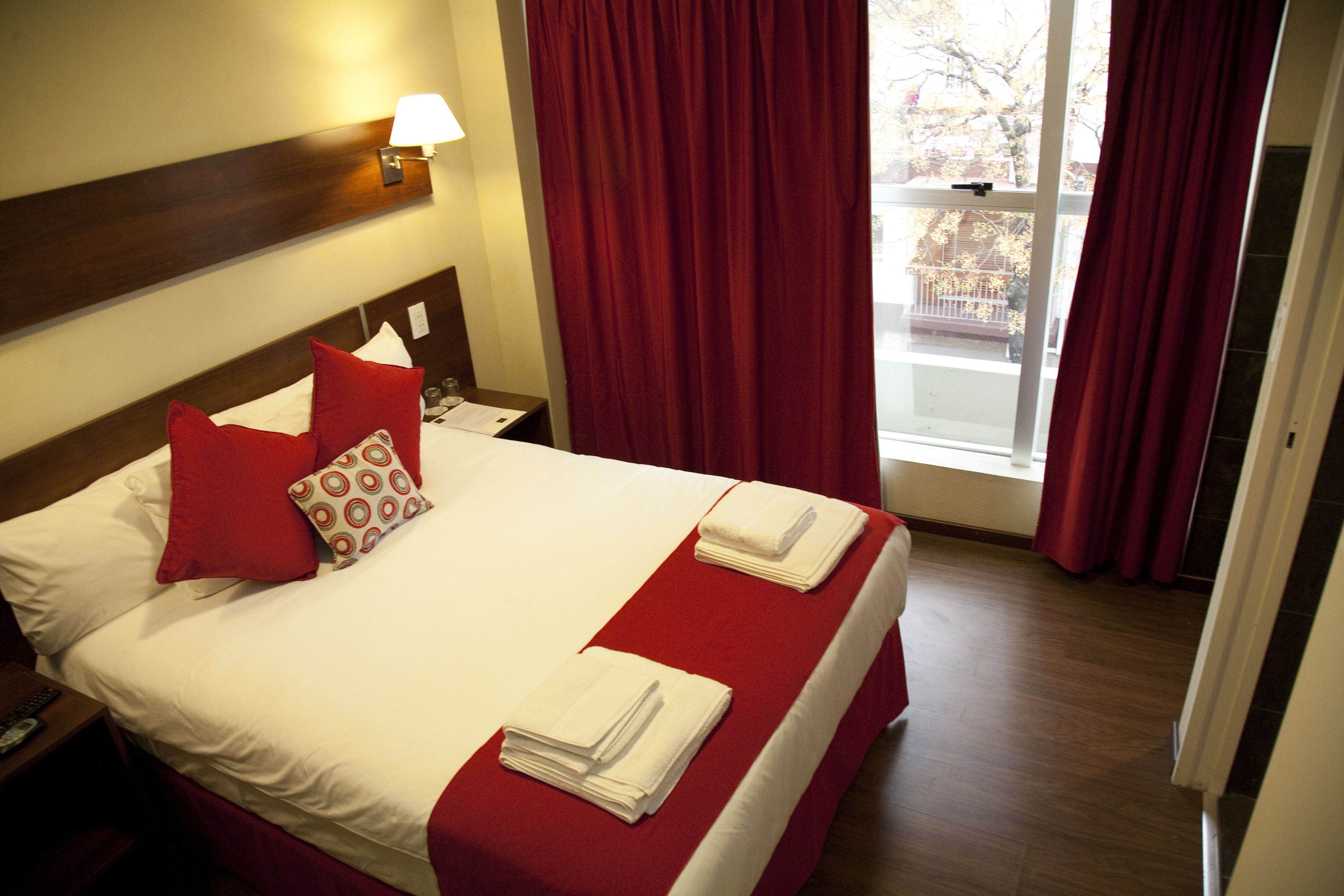 Une chambre d’hôtel avec un lit, des rideaux rouges, une table de chevet et une lampe.
