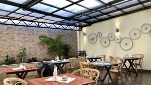 An outdoor patio area with tables and wicker chairs, a brick wall, and a ceiling with skylights. - First Palermo Viejo Hotel (Buenos Aires)