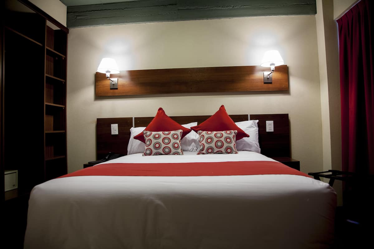 A neatly made bed with a red and white bedspread and matching pillows, two bedside lamps, and a wooden headboard.