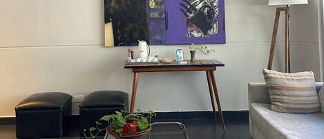 Un salon moderne avec un canapé d’angle, une table basse en verre et un tableau abstrait accroché au mur.