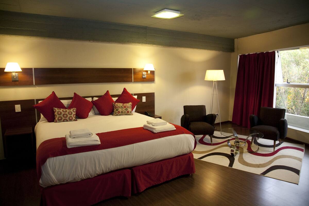 A hotel room with a large bed, two chairs, a desk, and a window with curtains.