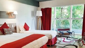 A hotel room with two beds, a large window with red curtains, a standing lamp, and a view of greenery outside. - First Palermo Viejo Hotel (Buenos Aires)