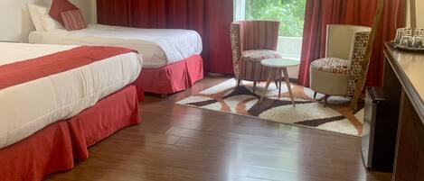 Habitación de hotel con dos camas, una mesita, una silla y una ventana con cortinas.