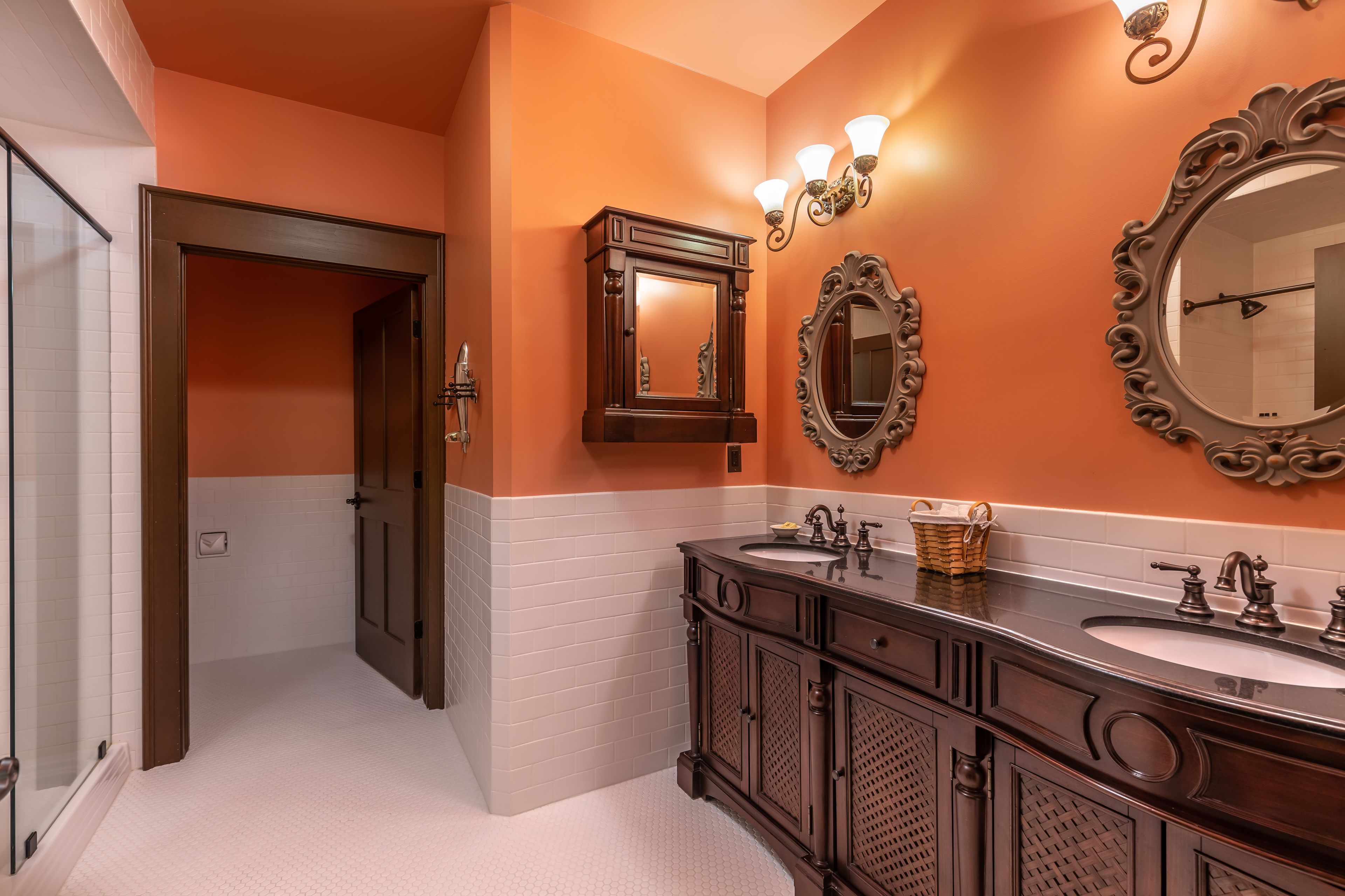 Une salle de bain avec deux lavabos, un miroir et une porte donnant sur une autre pièce.