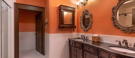 A bathroom with two sinks, a mirror, and a door leading to another room.