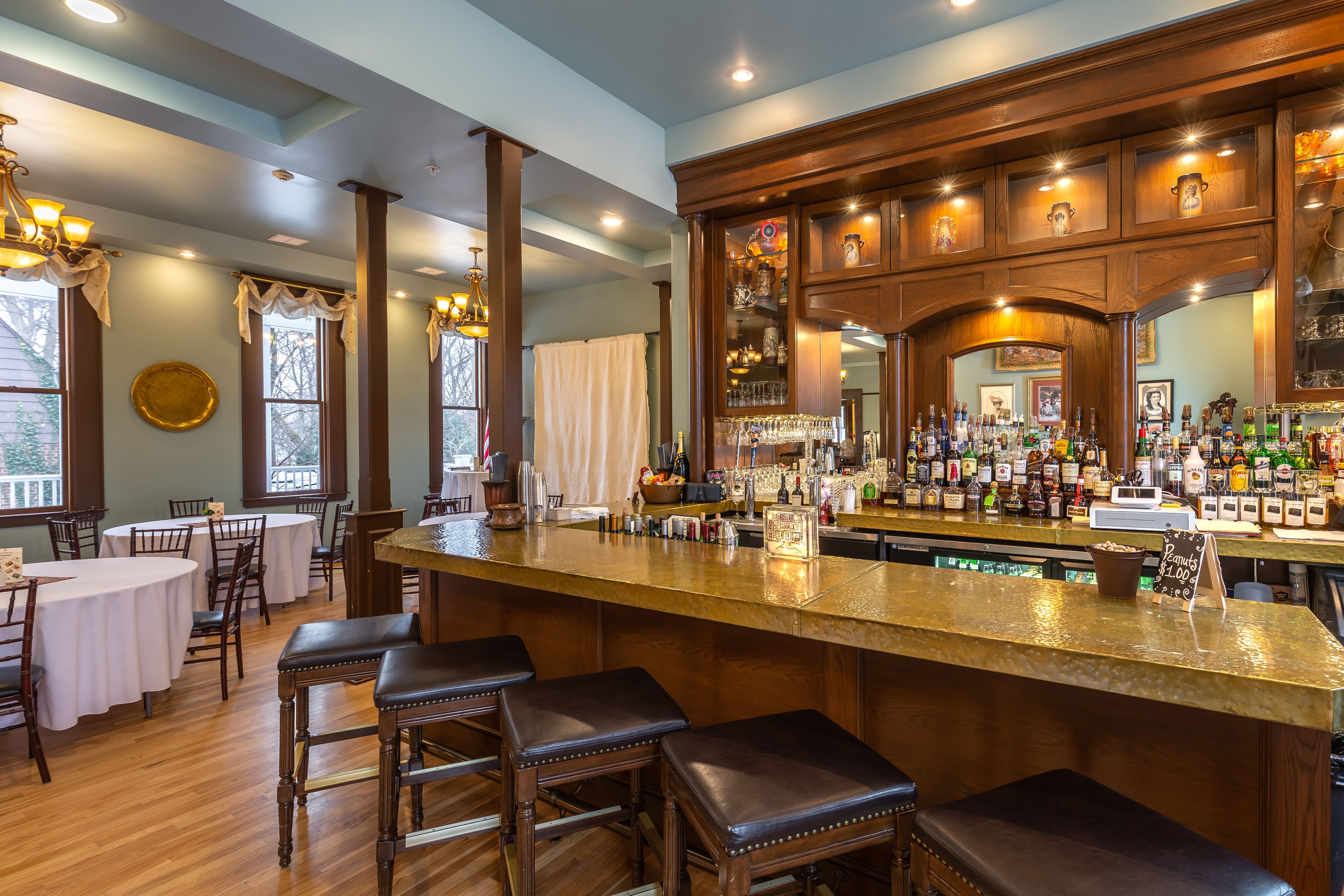 Zona de bar con mostrador de madera, taburetes y una variedad de botellas.