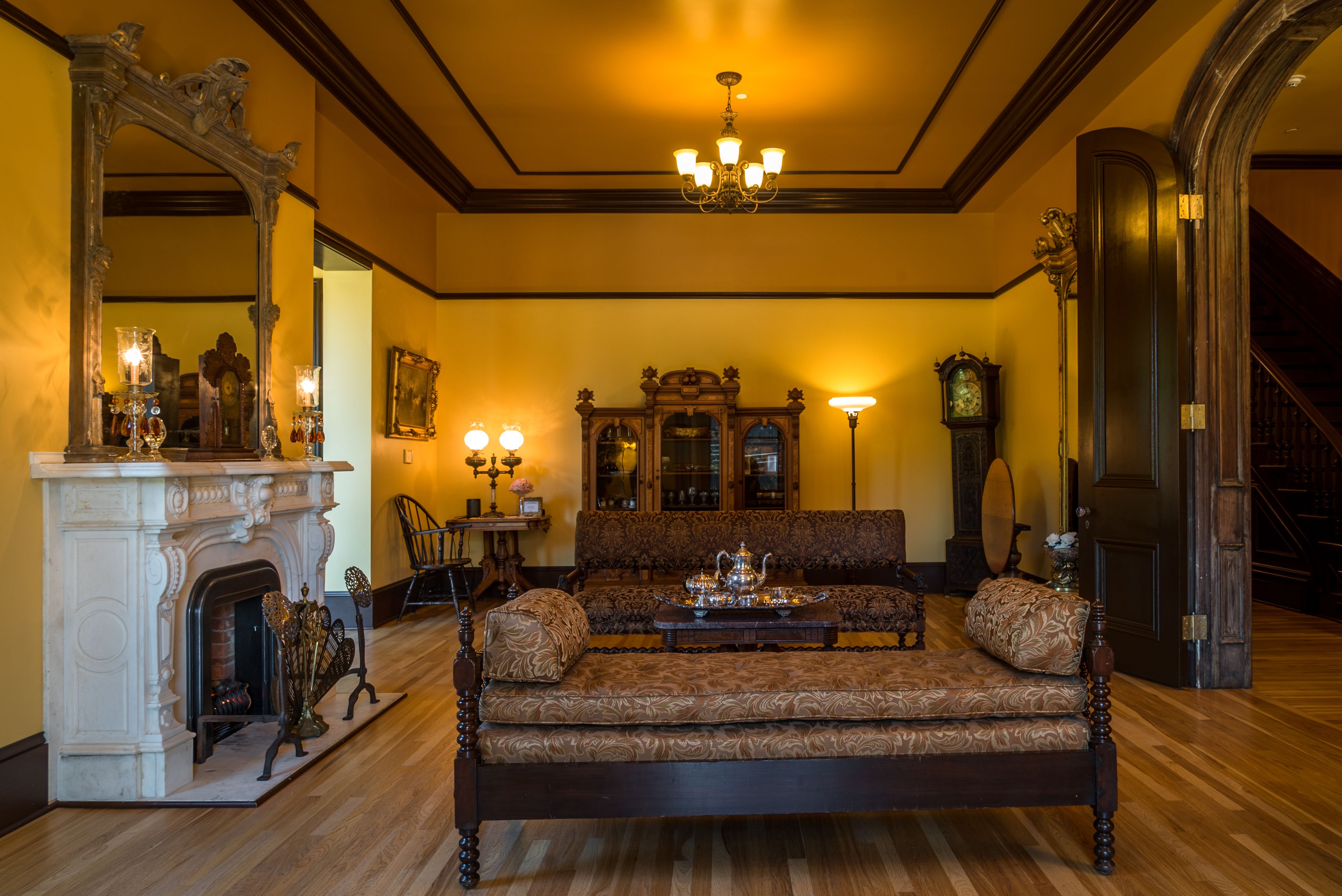 A grand room with a large ornate sofa, a fireplace, and a chandelier.