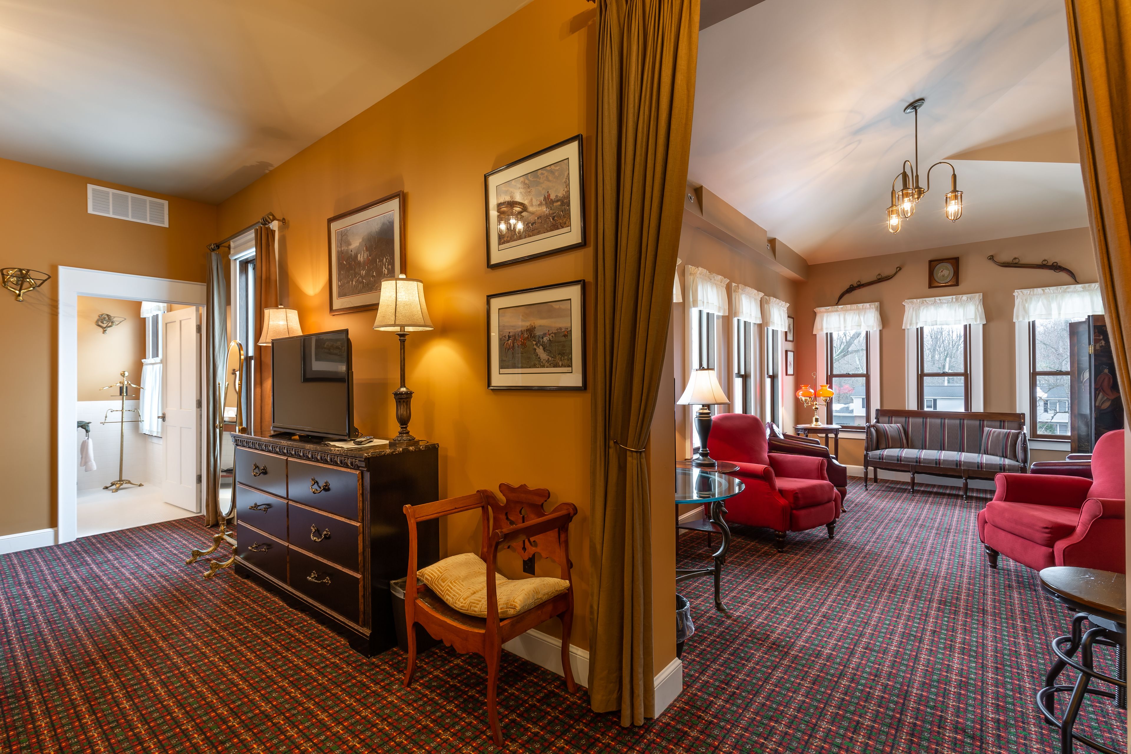 A hotel room with a patterned carpet, a wooden chair, a sofa, and a television on a dresser.