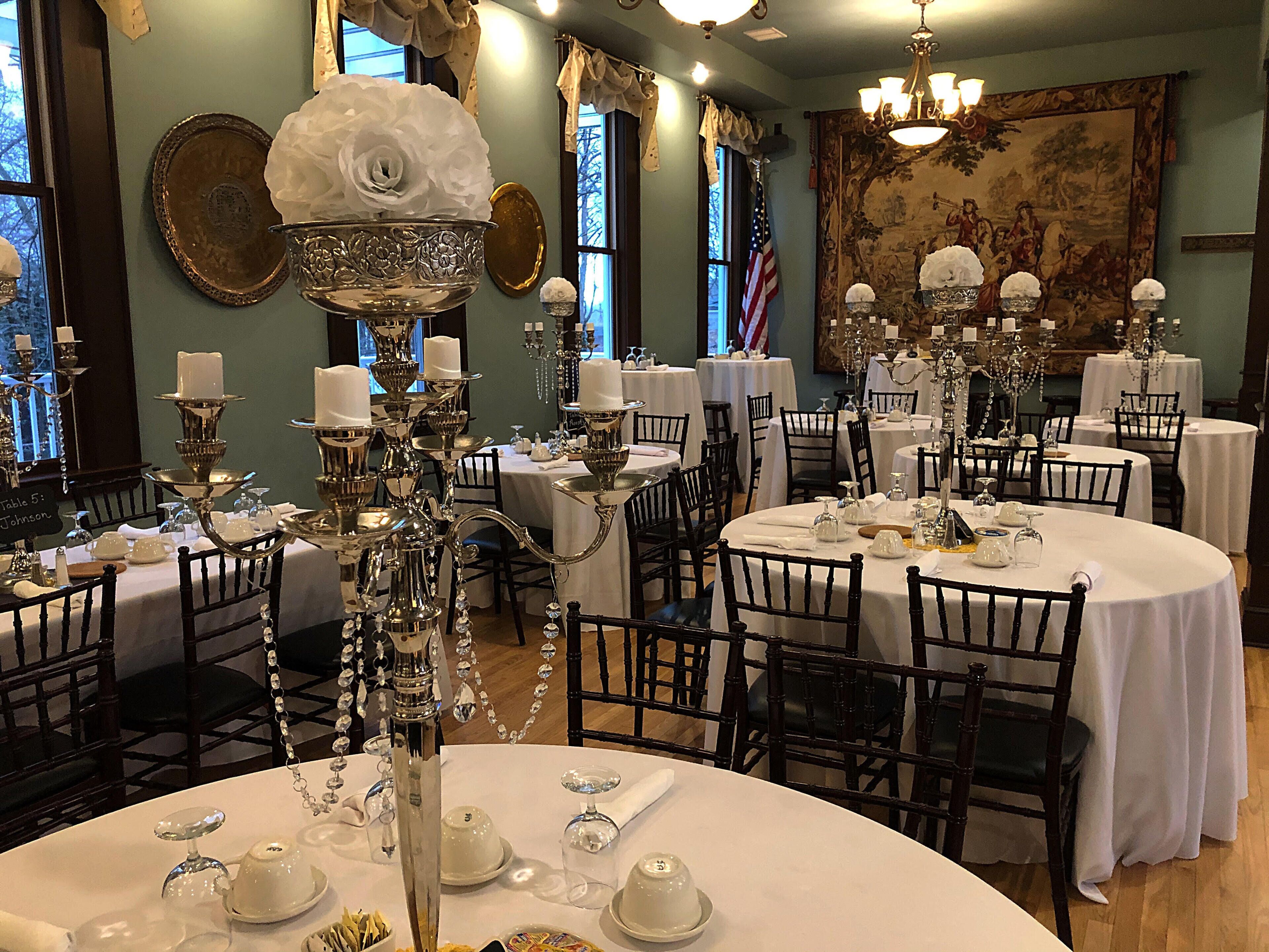 A formal dining room with round tables, white tablecloths, and ornate silver candelabras.
