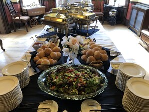 A buffet setup with various food items, including a large salad bowl, rolls, and multiple serving dishes. - Steele Mansion (Painesville)