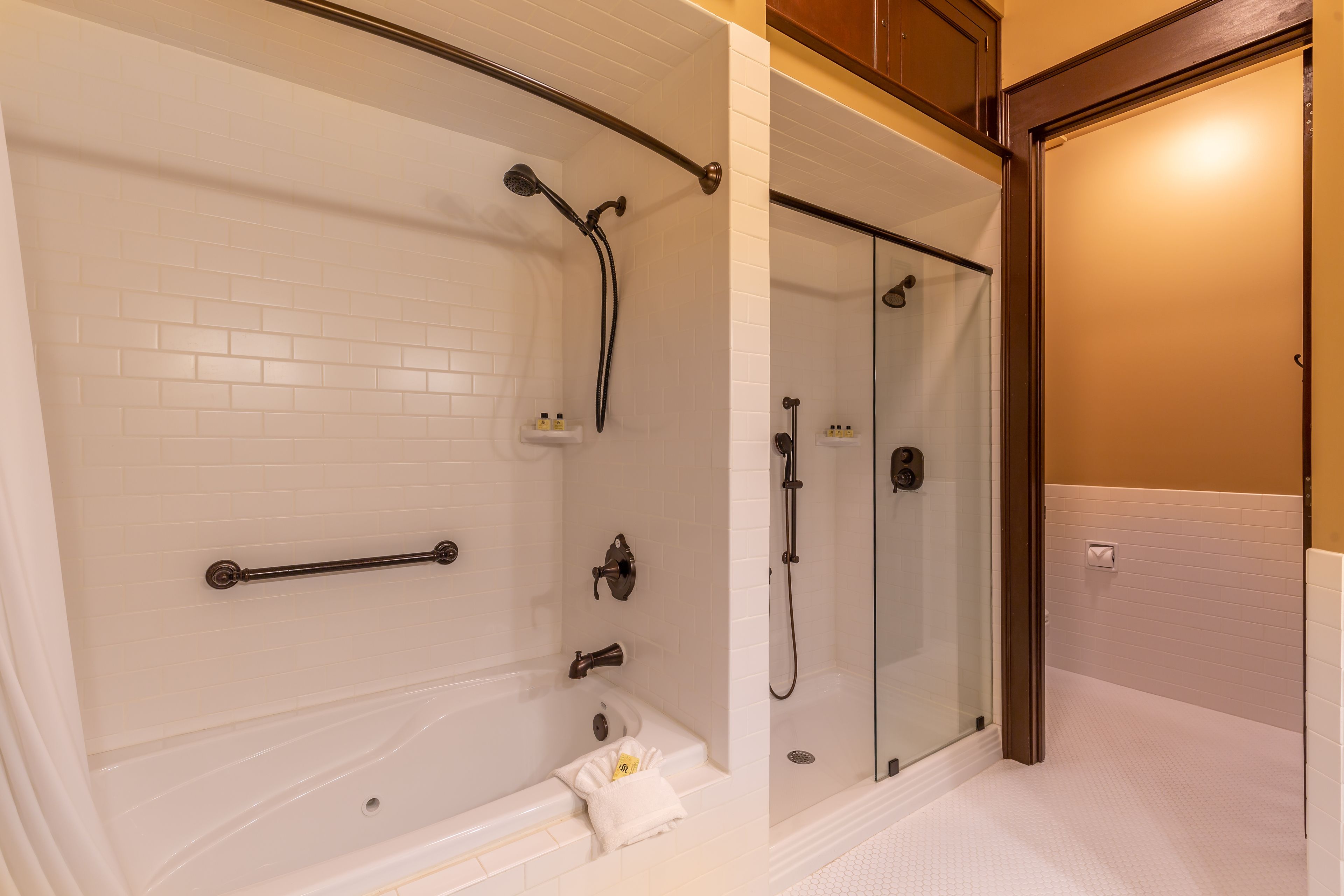 A modern bathroom with a glass-enclosed shower, a white bathtub, and a white tiled floor.