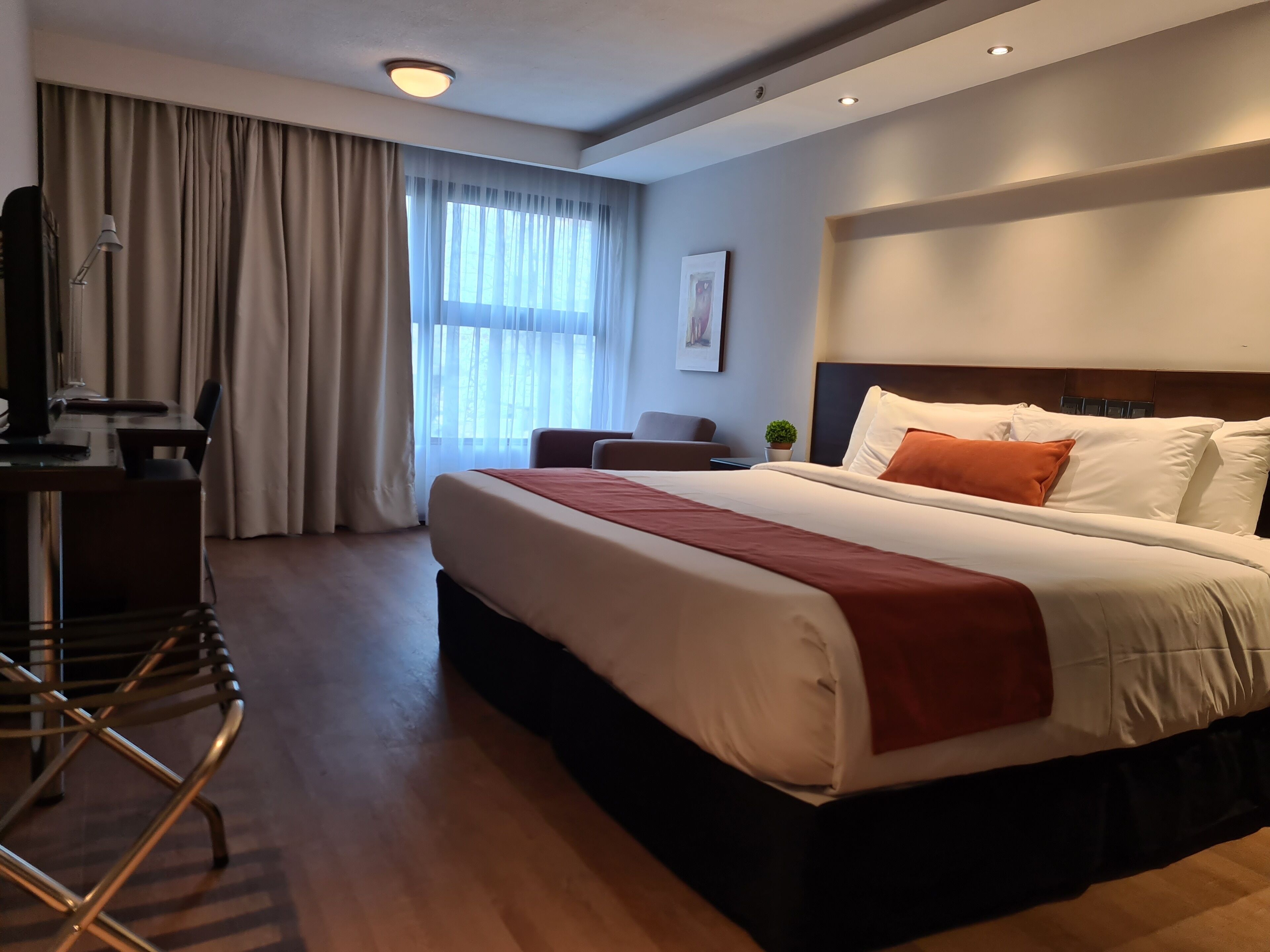 Una habitación de hotel con una cama grande, un escritorio con silla, una mesita y una ventana con cortinas.