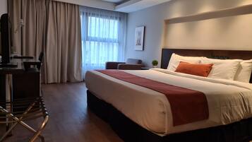 Una habitación de hotel con una cama grande, un escritorio con silla, una mesita y una ventana con cortinas.