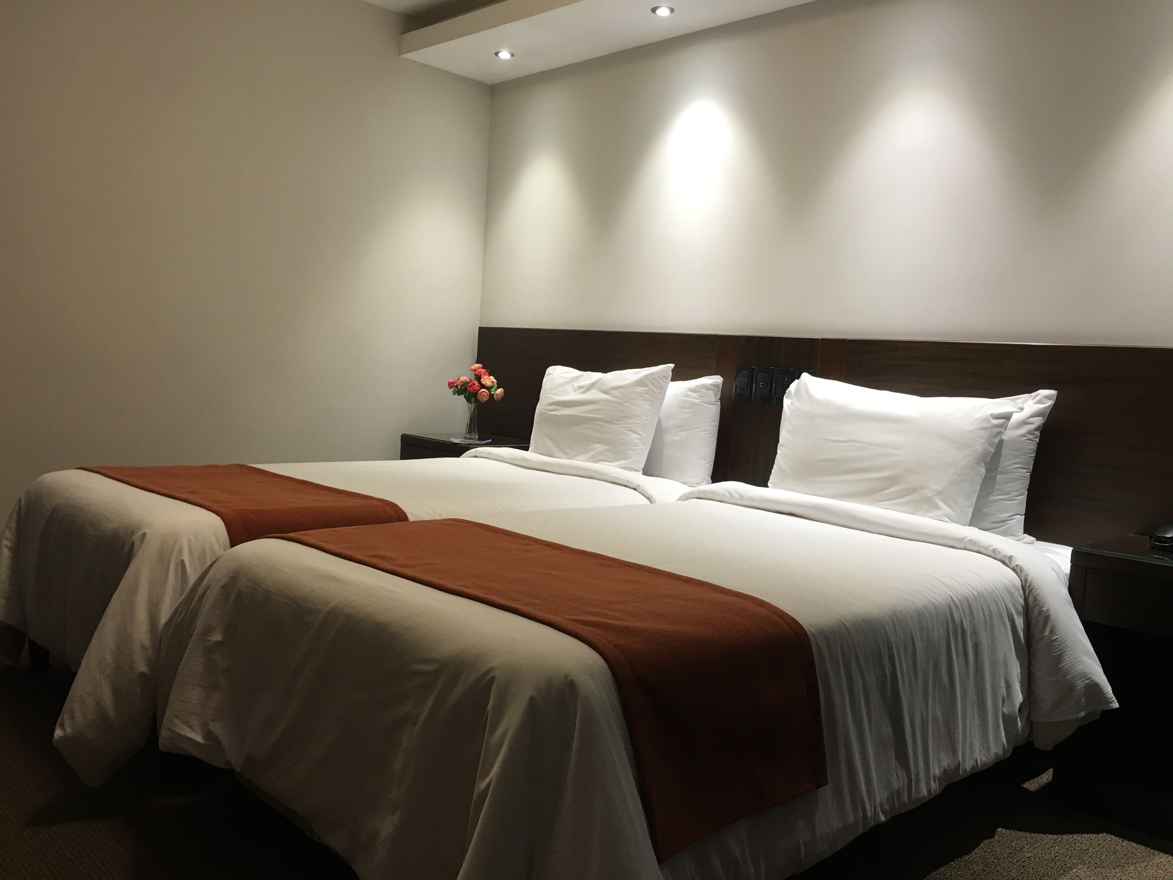 A hotel room with two beds, a nightstand, and a vase of flowers.