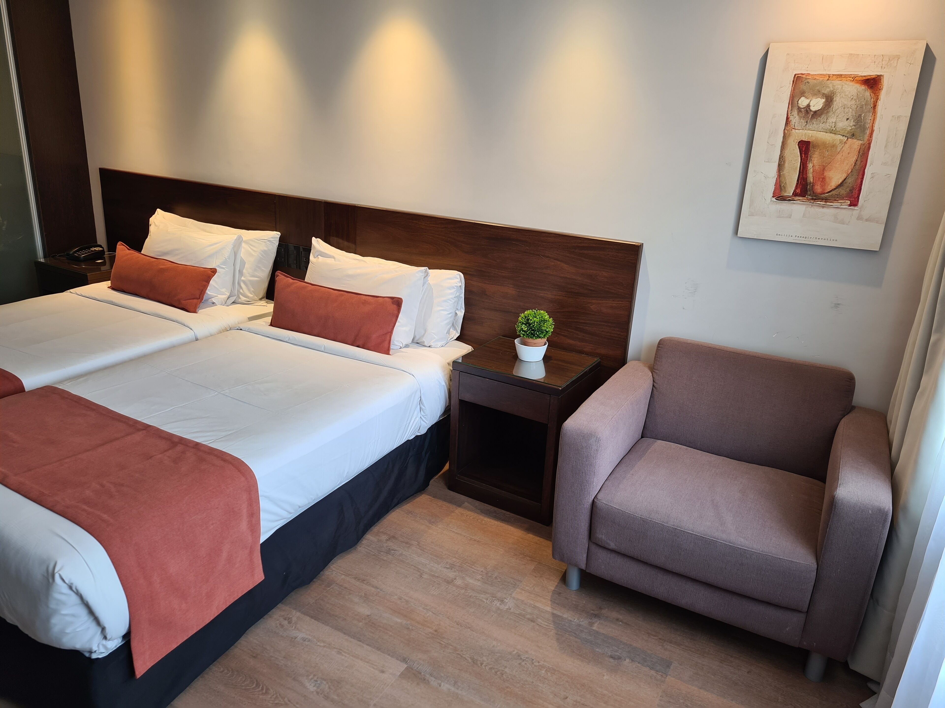 Een hotelkamer met twee bedden, een nachtkastje, een stoel en een kleine potplant.