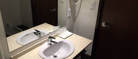 Un bagno con due lavandini, uno specchio, un asciugacapelli e un portascopevoli.