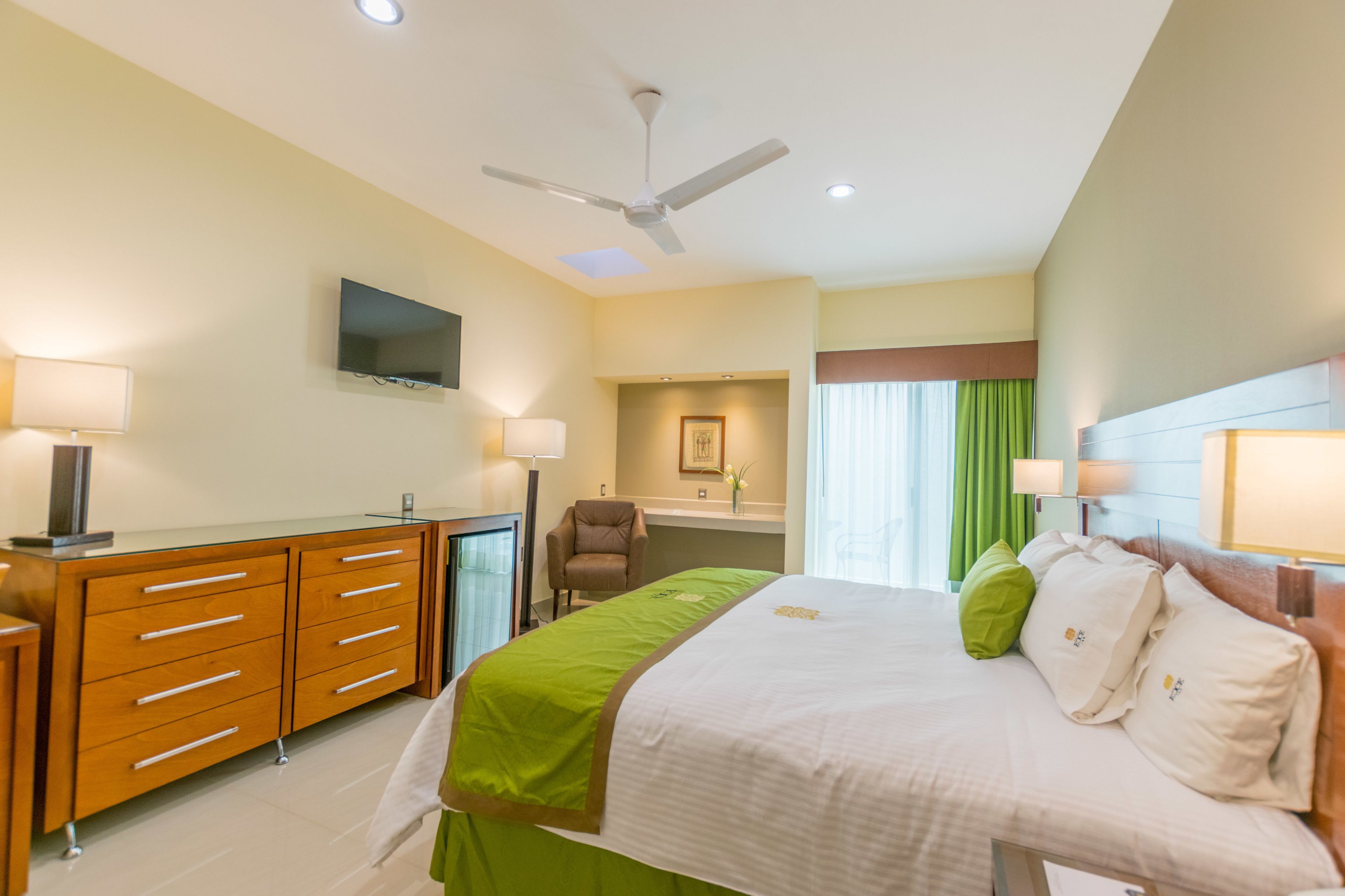 A hotel room with a bed, a desk, a chair, a television, and a ceiling fan.
