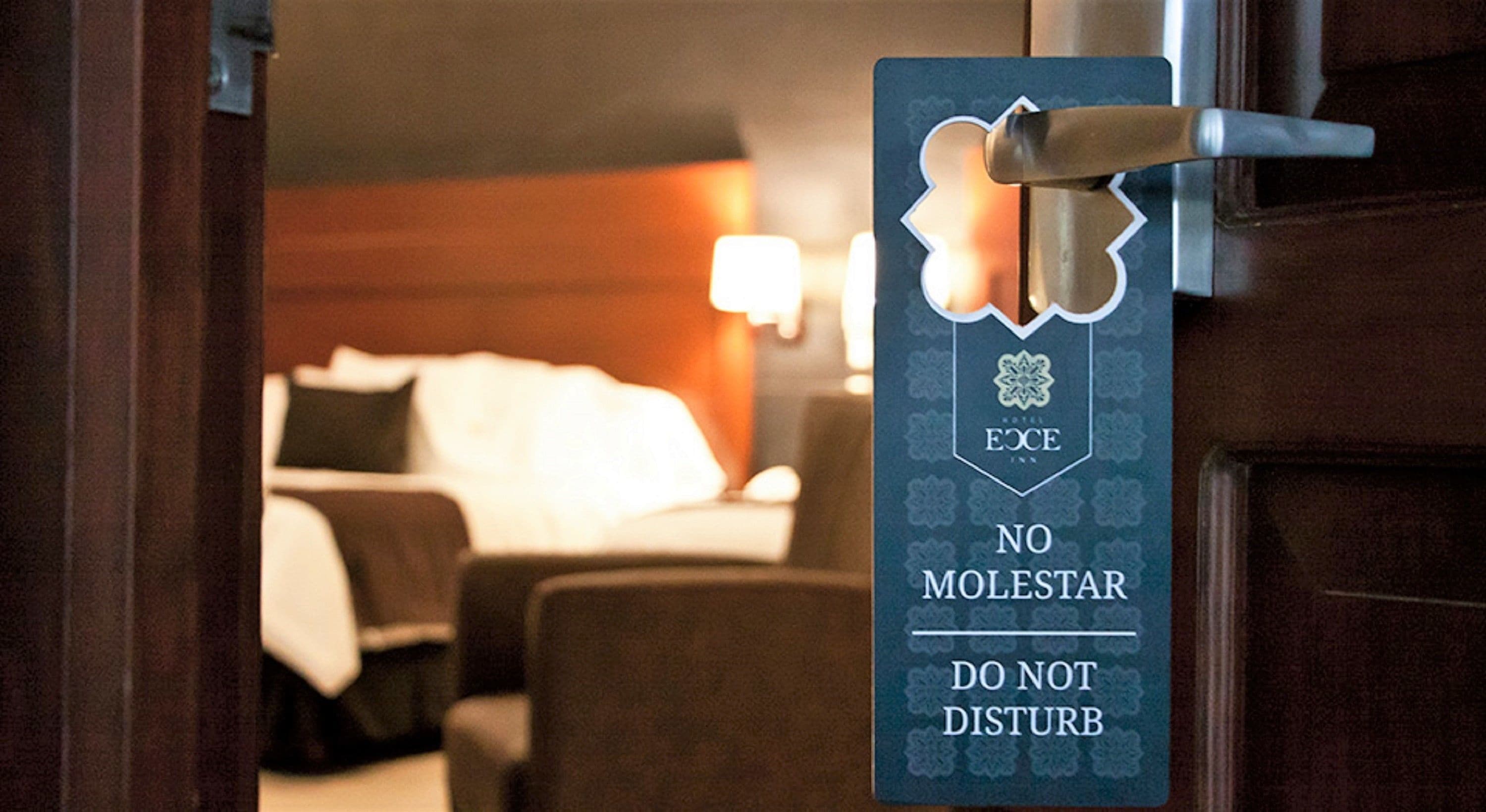 A hotel room door with a sign that reads "ECCE INN NO MOLESTAR DO NOT DISTURB".