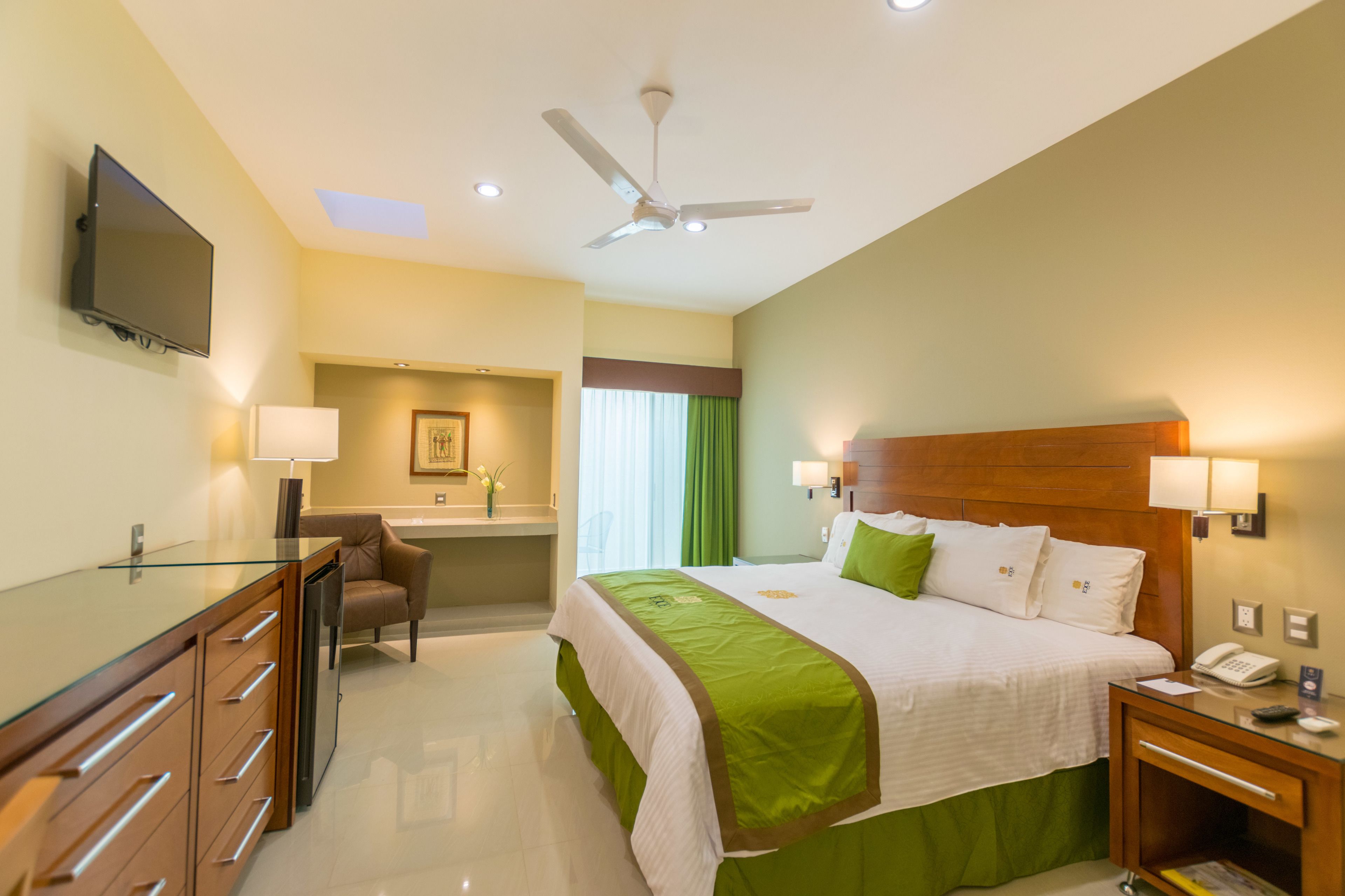 Una habitación de hotel con cama, escritorio, silla, televisor y ventilador de techo.