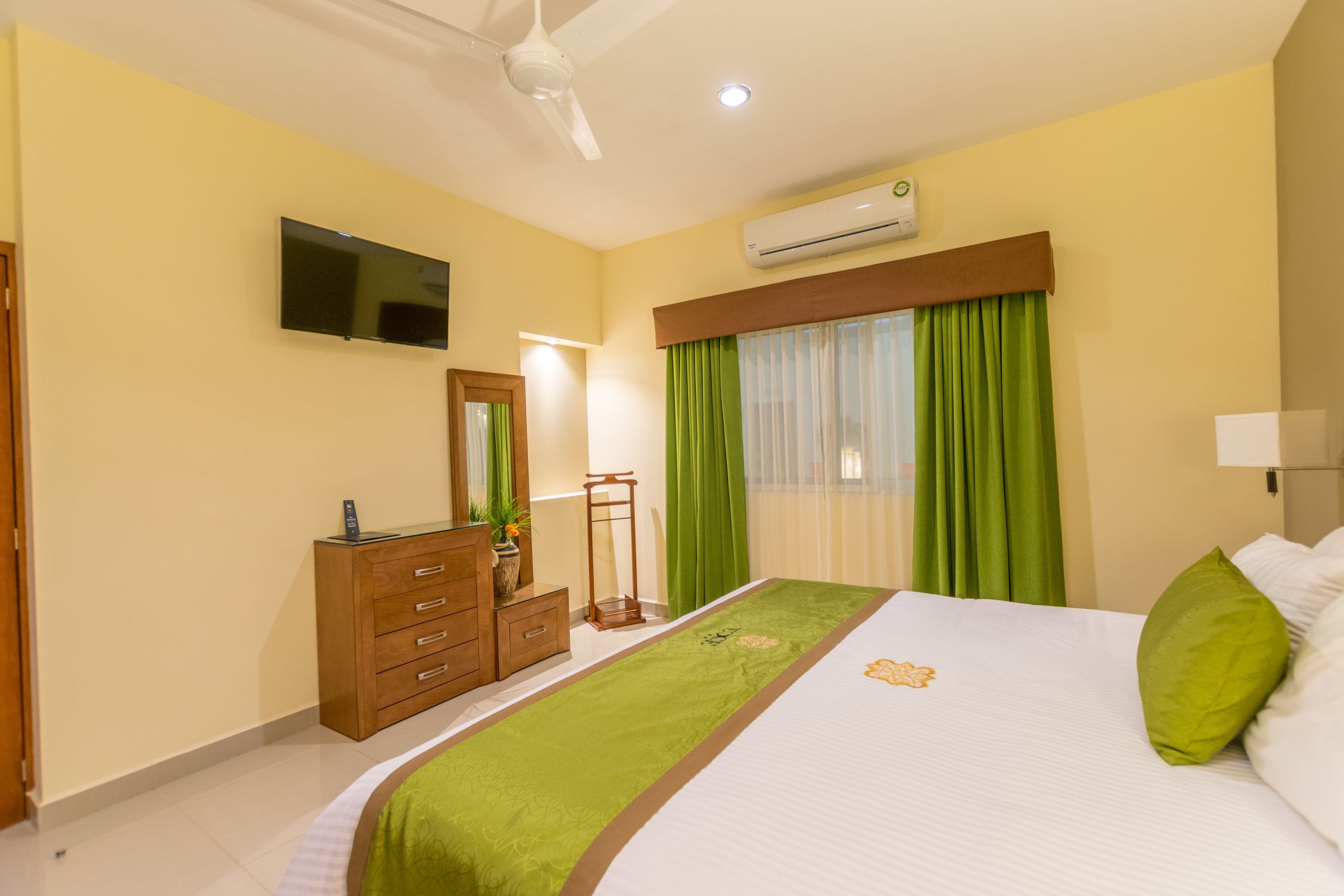 A hotel room with a bed, a TV, a dresser, a mirror, and an air conditioning unit.