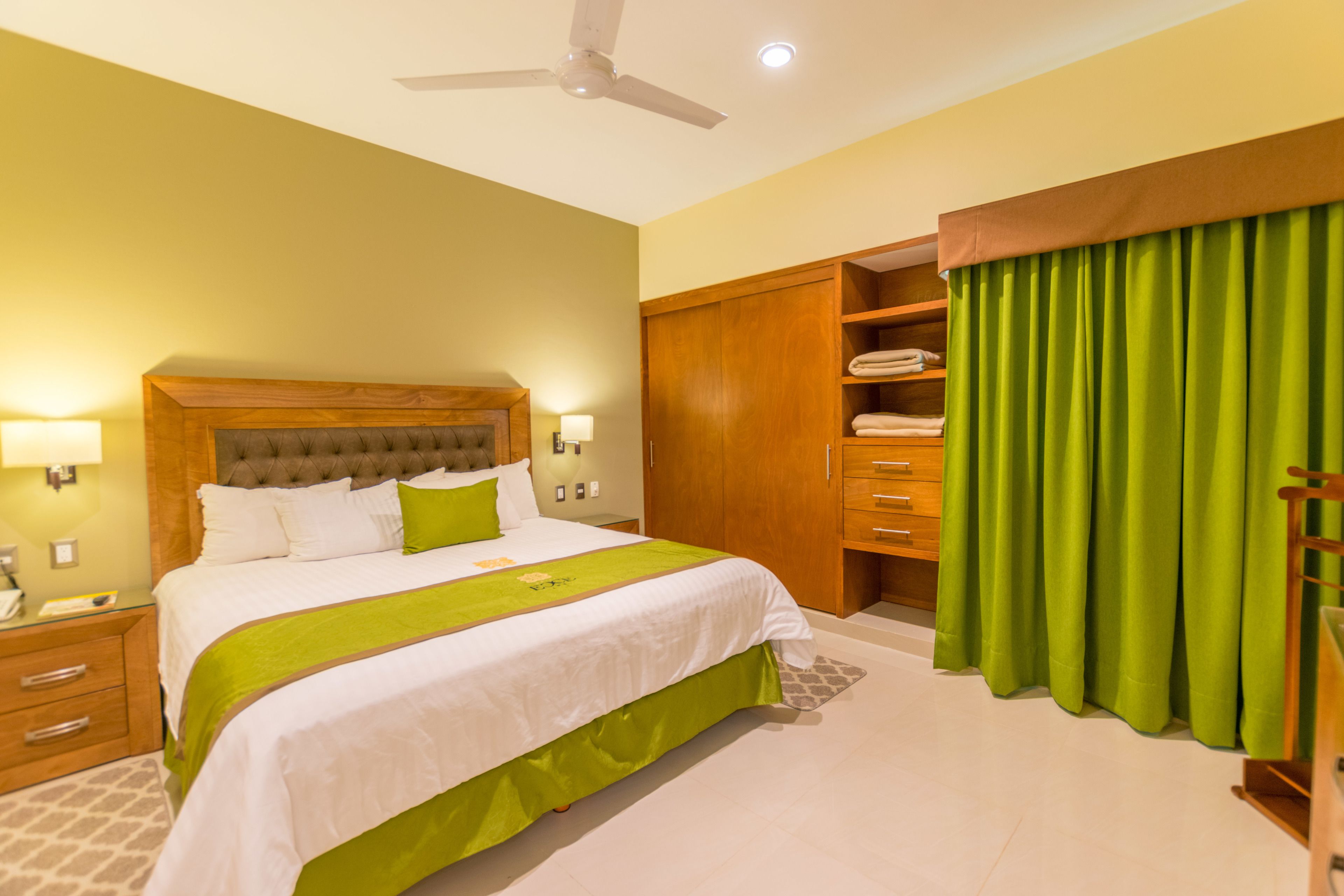 A neatly arranged hotel room with a bed, bedside tables, a wardrobe, and a green curtain.