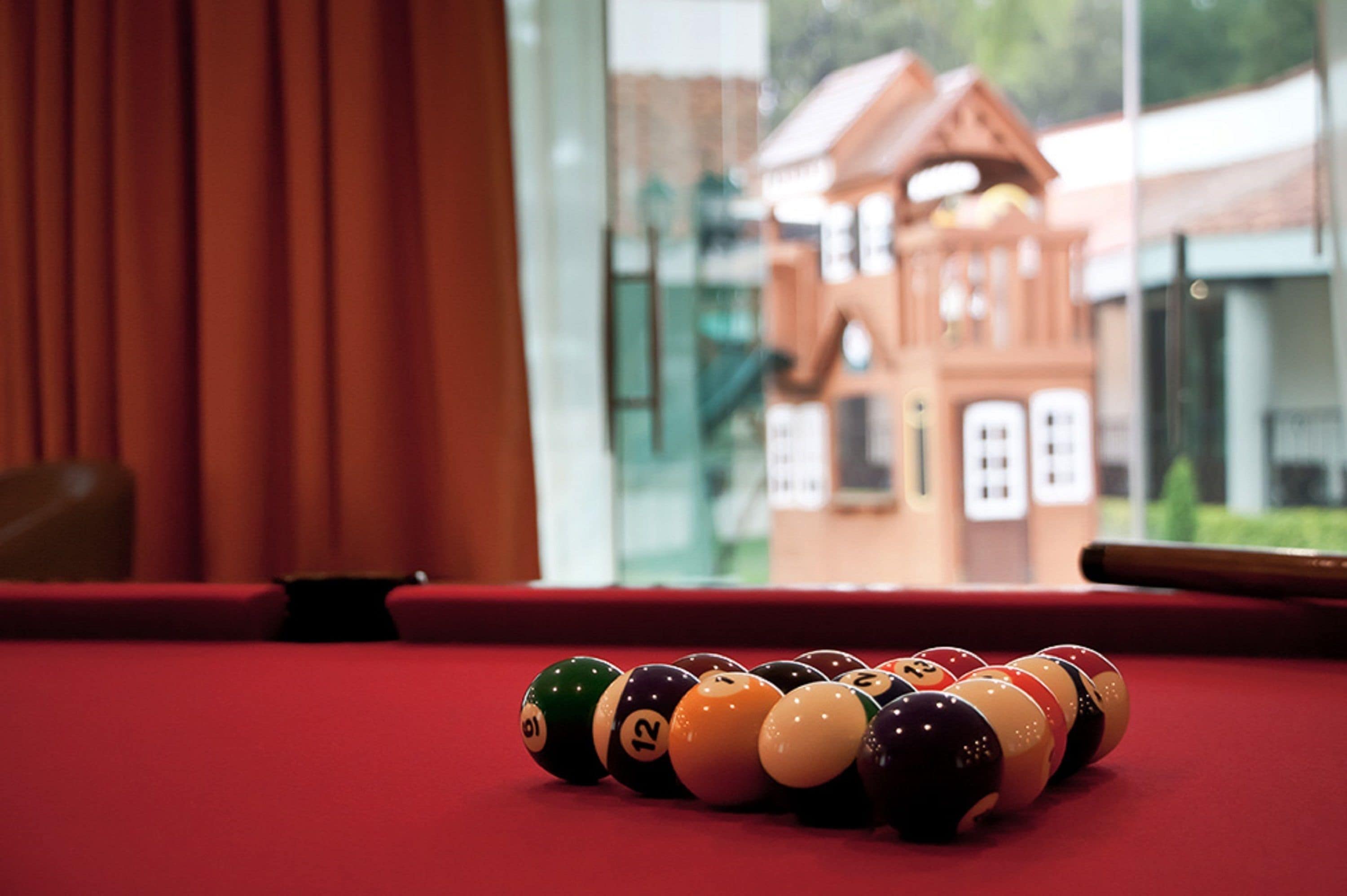 A pool table with billiard balls in front of a window with a view of a building.