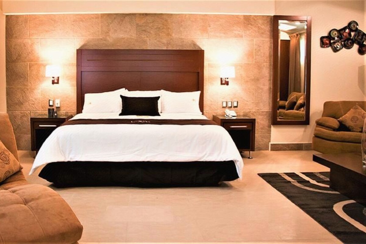 A hotel room with a large bed, two bedside tables, a sofa, and a mirror.