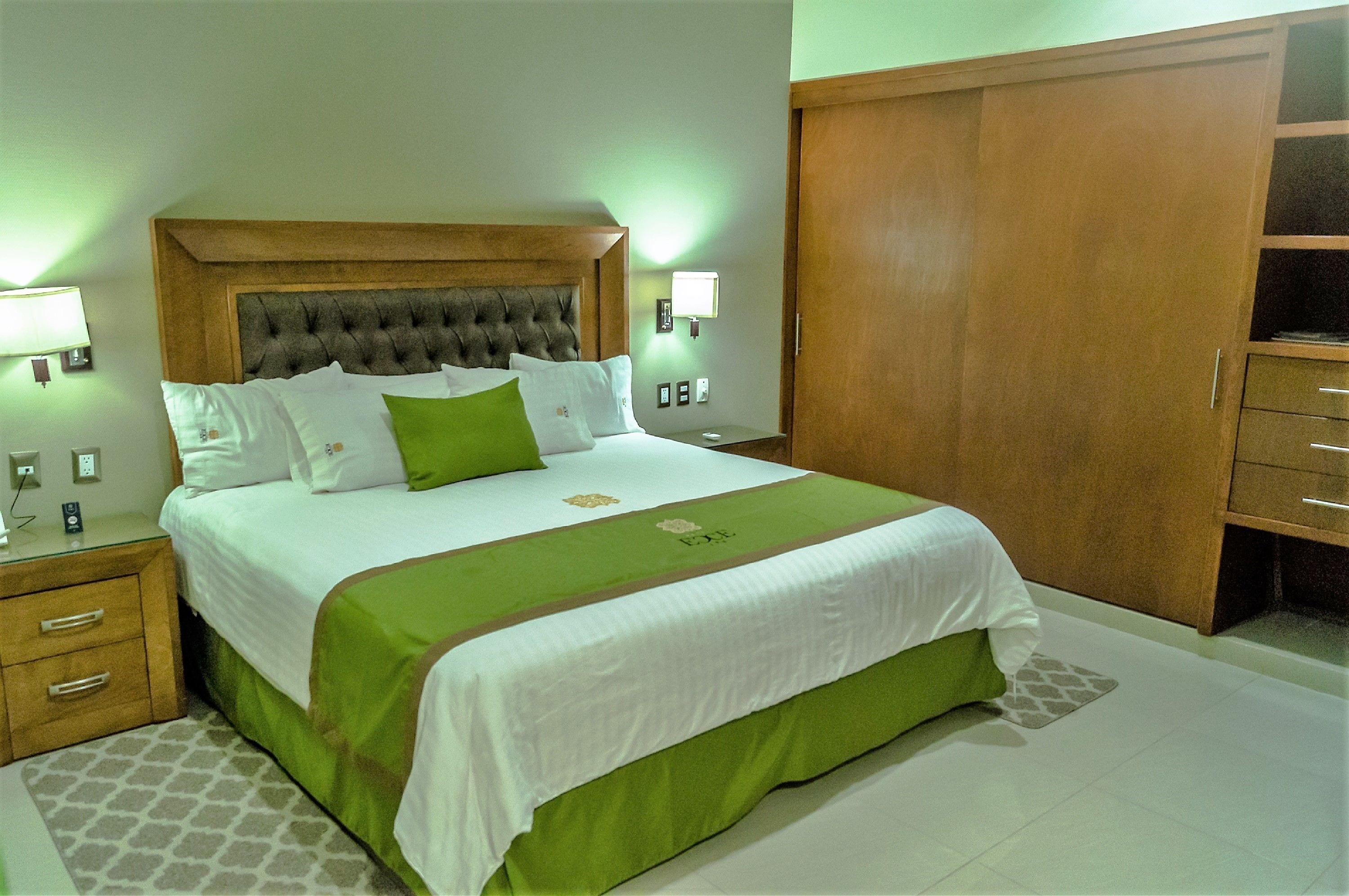 A neatly made bed with a green and white bedspread, a wooden headboard, and bedside lamps.