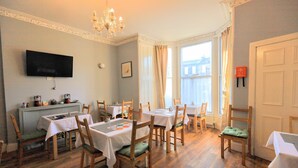 A dining area with multiple tables and chairs, a chandelier, a television on the wall, and a window with curtains. - Edinburgh Holiday Guest House (Edinburgh)