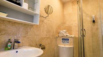 Een badkamer met een wastafel, toilet en douche. Er hangt een berichtje op de toiletwand.