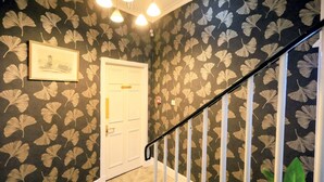 A hallway with a patterned wallpaper, a white door, and a staircase with white railings. - Edinburgh Holiday Guest House (Edinburgh)