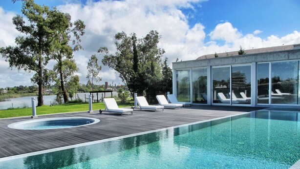 A modern outdoor swimming pool with clear blue water, surrounded by wooden decking and white lounge chairs. - Faros de Carrasco Apartments (Paso de Carrasco)