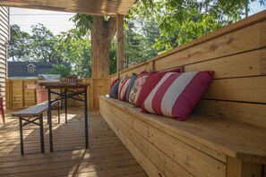 A wooden deck with a bench and a table, surrounded by trees.