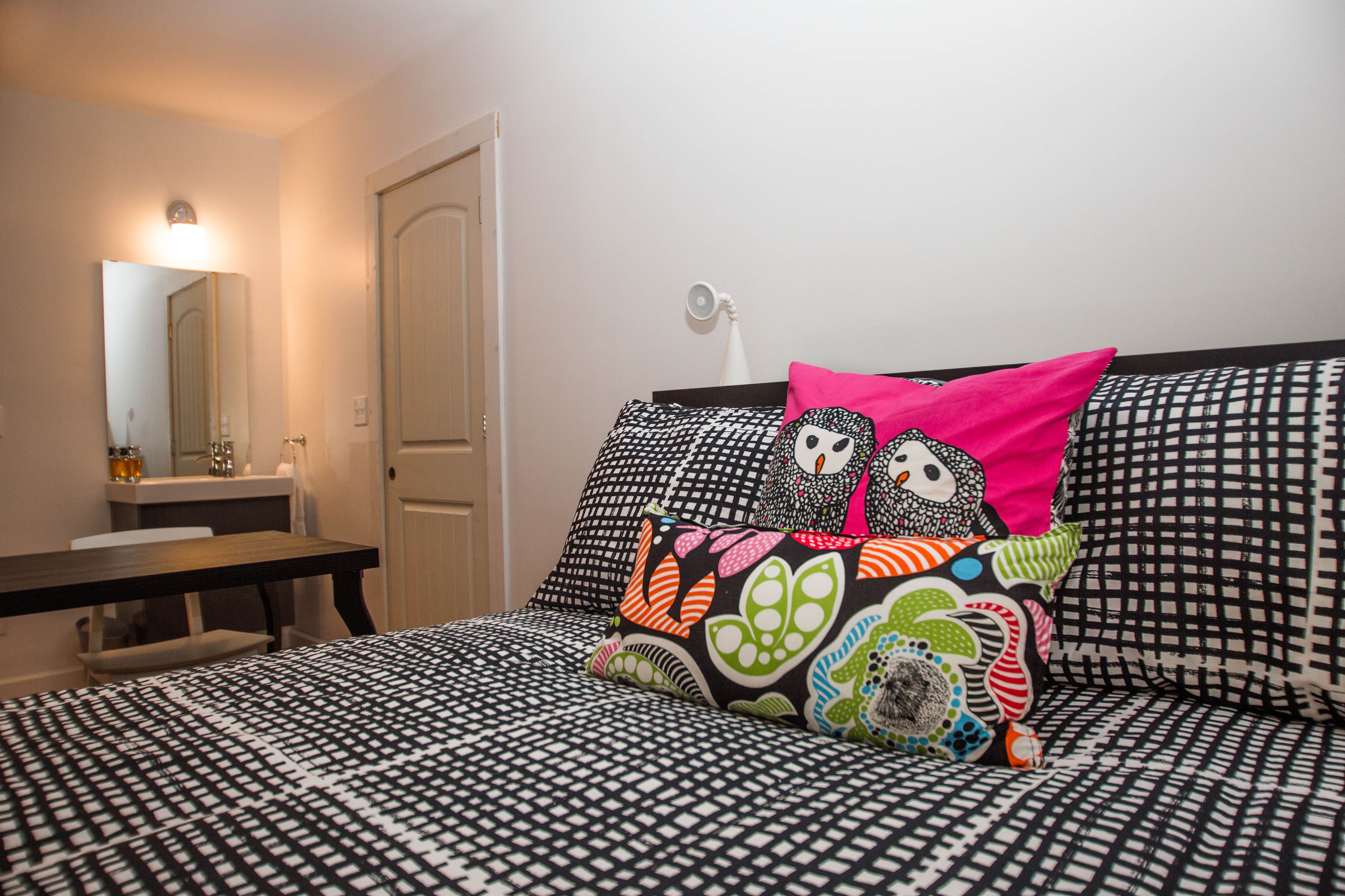 A bedroom with a patterned bedspread, a bedside table, a mirror, and a door.