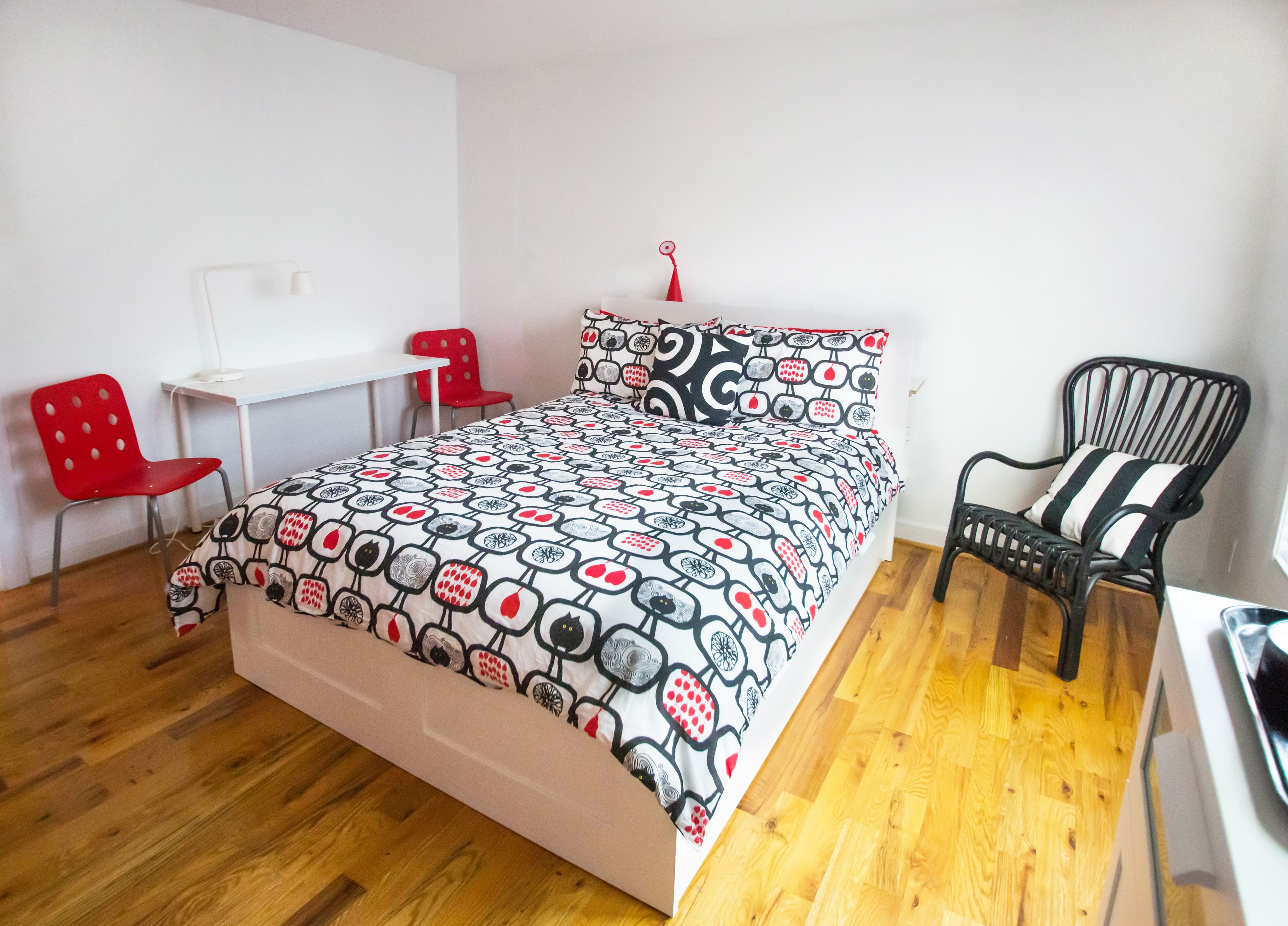 A bedroom with a bed, a desk, a red chair, and a black chair.