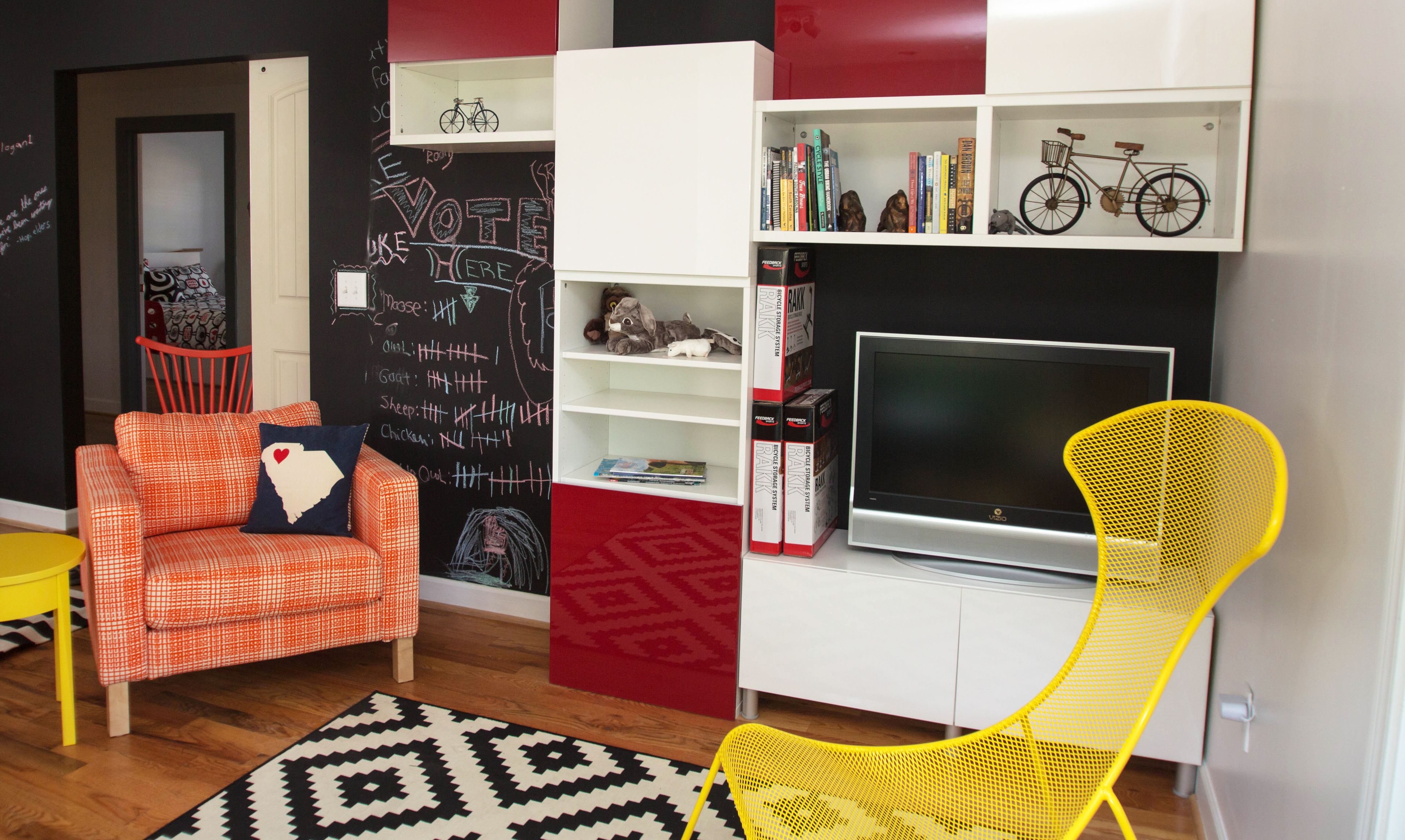 A modern living room with a red and white sofa, a yellow chair, a bookshelf with books and a bicycle, and a TV on a white cabinet.