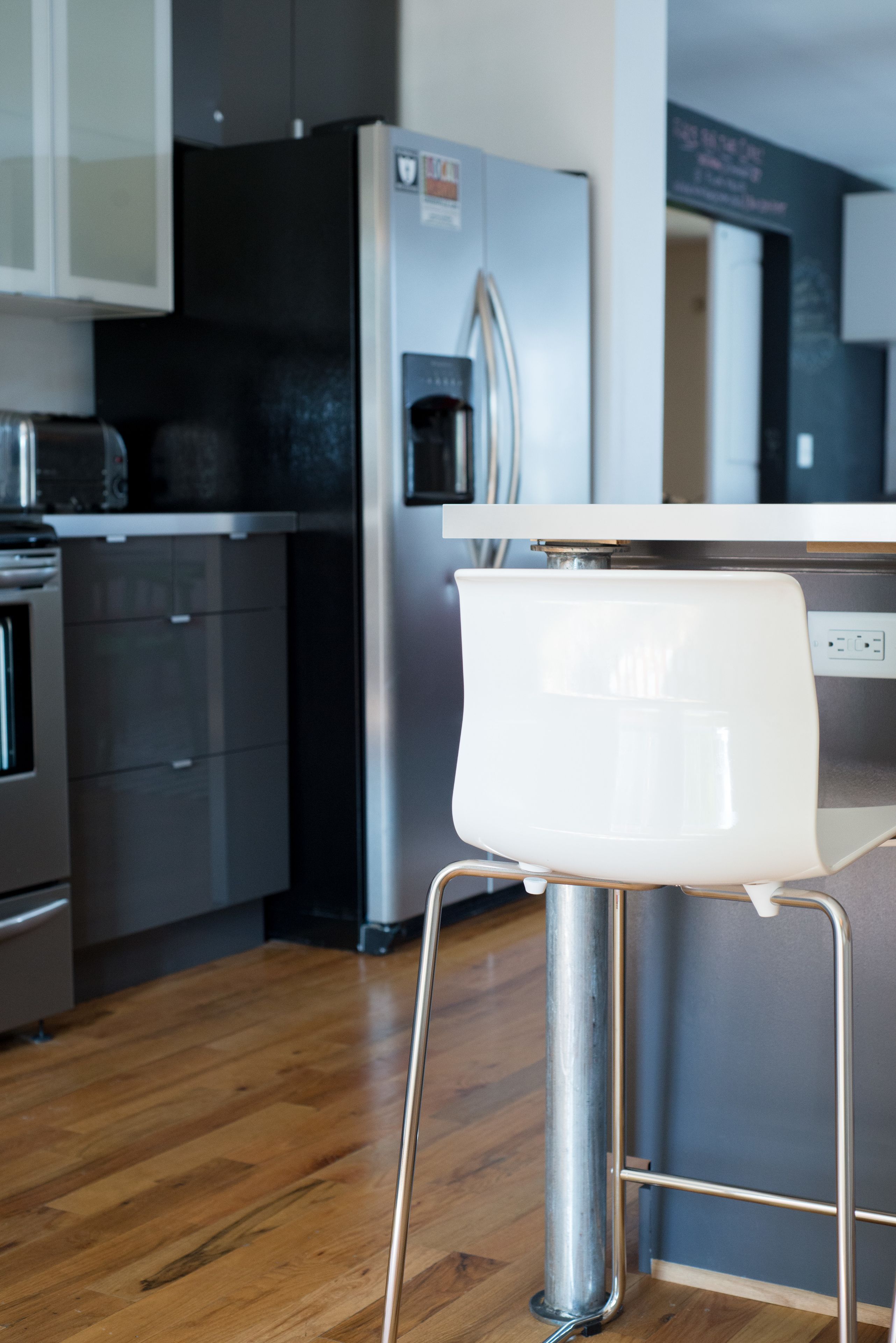 A modern kitchen with stainless steel appliances, a wooden floor, and a white chair.