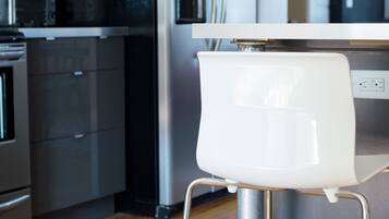 A modern kitchen with stainless steel appliances, a wooden floor, and a white chair.